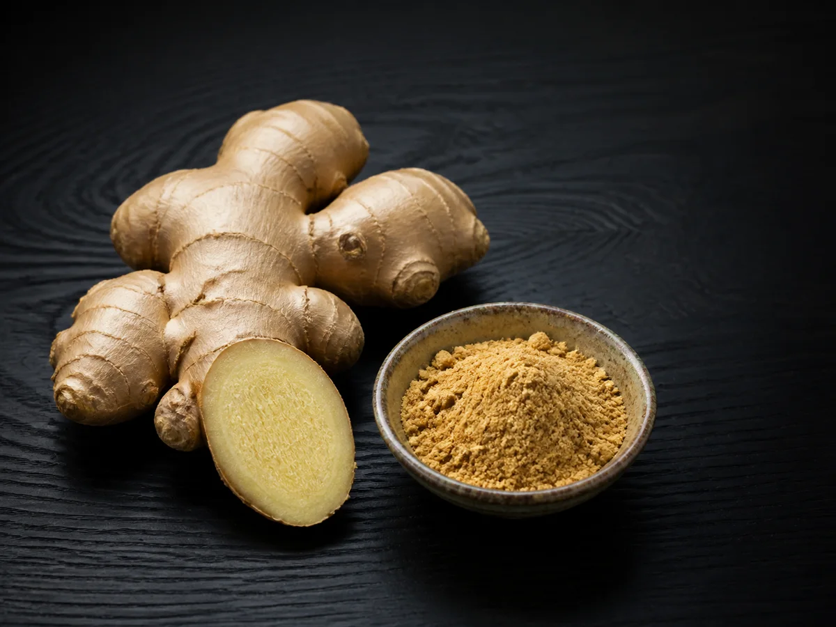 Fresh ginger and ground ginger powder on dark wood