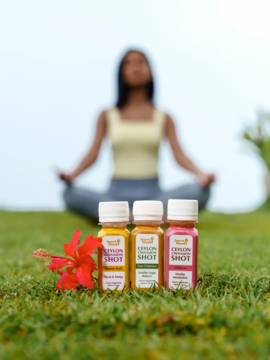 Three Sweet Wood Ceylon Cinnamon Shot bottles with plain white caps in front of a woman meditating outdoors