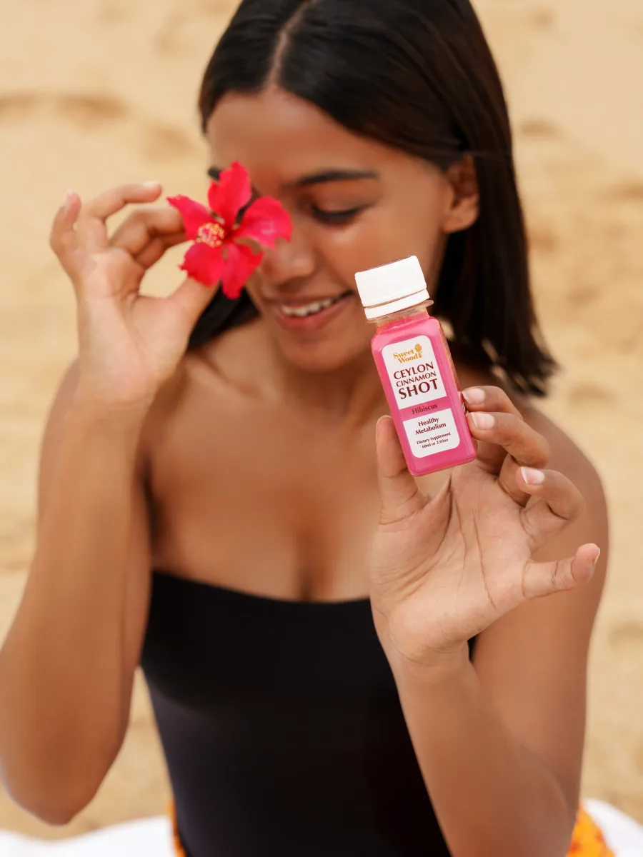 Woman holding a Sweet Wood Ceylon Cinnamon and Hibiscus Shot with a plain white cap