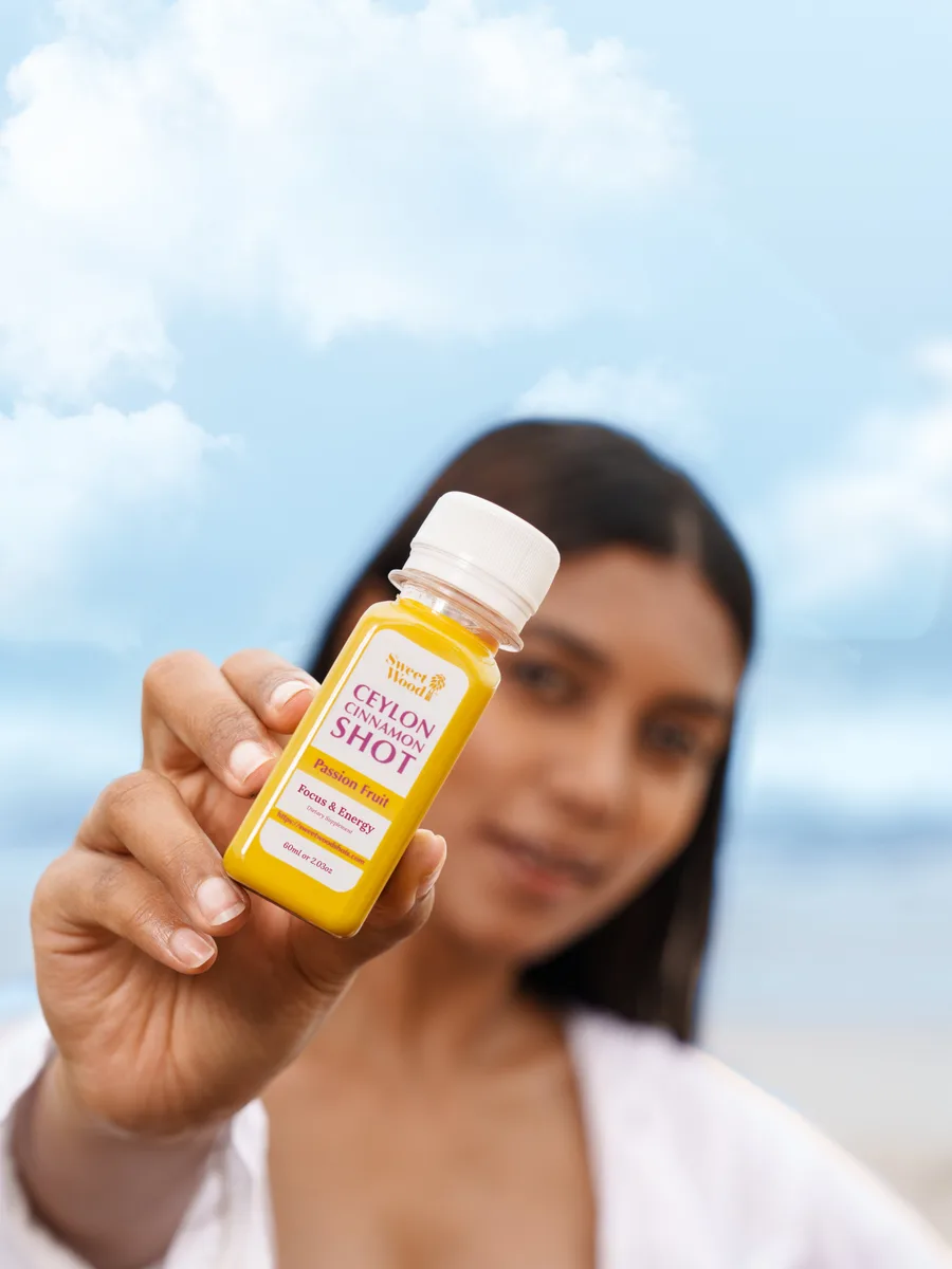 Woman holding an English-label Sweet Wood Passion Fruit Ceylon Cinnamon Shot with a plain white cap outdoors