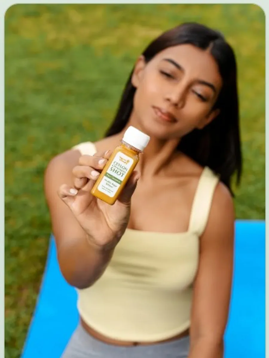 Woman seated outdoors holding a Sweet Wood Pure Ceylon Cinnamon Shot toward the camera