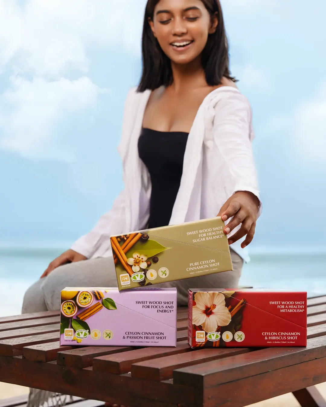 Woman presenting three Sweet Wood shot boxes on a table at the beach