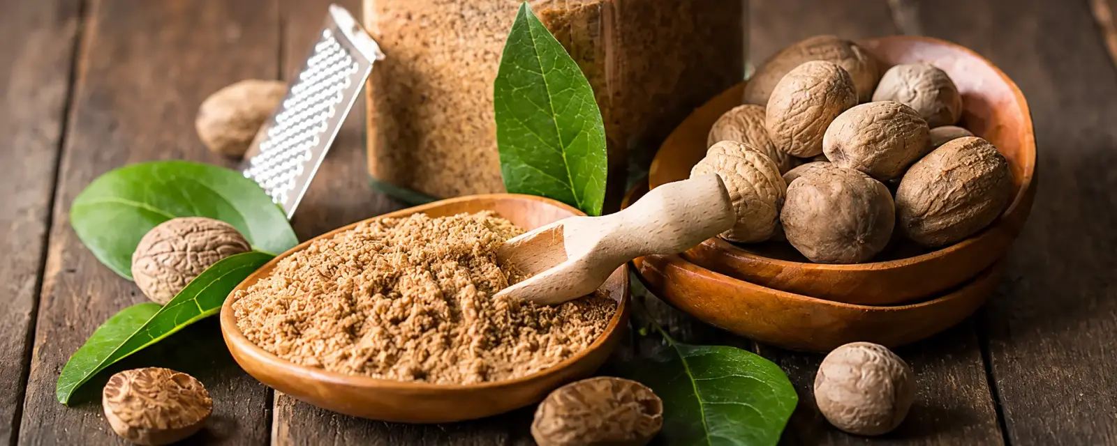 Whole nutmeg seeds and ground nutmeg with fresh leaves over rustic wood