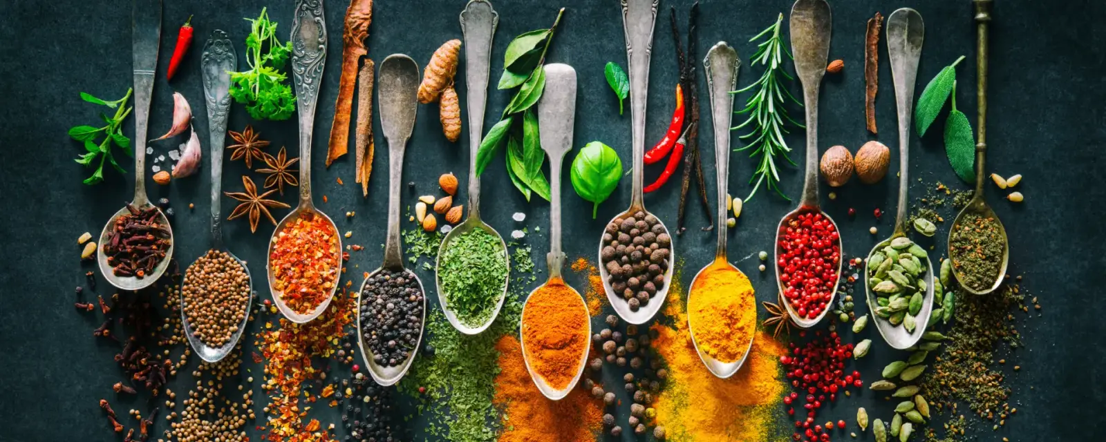 A wide assortment of whole and ground spices arranged in vintage spoons