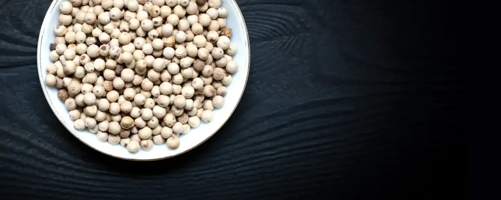 White peppercorns in a bowl on dark charred wood